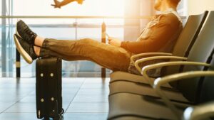 A traveler resting their feet on a suitcase at the airport, a plane taking off outside